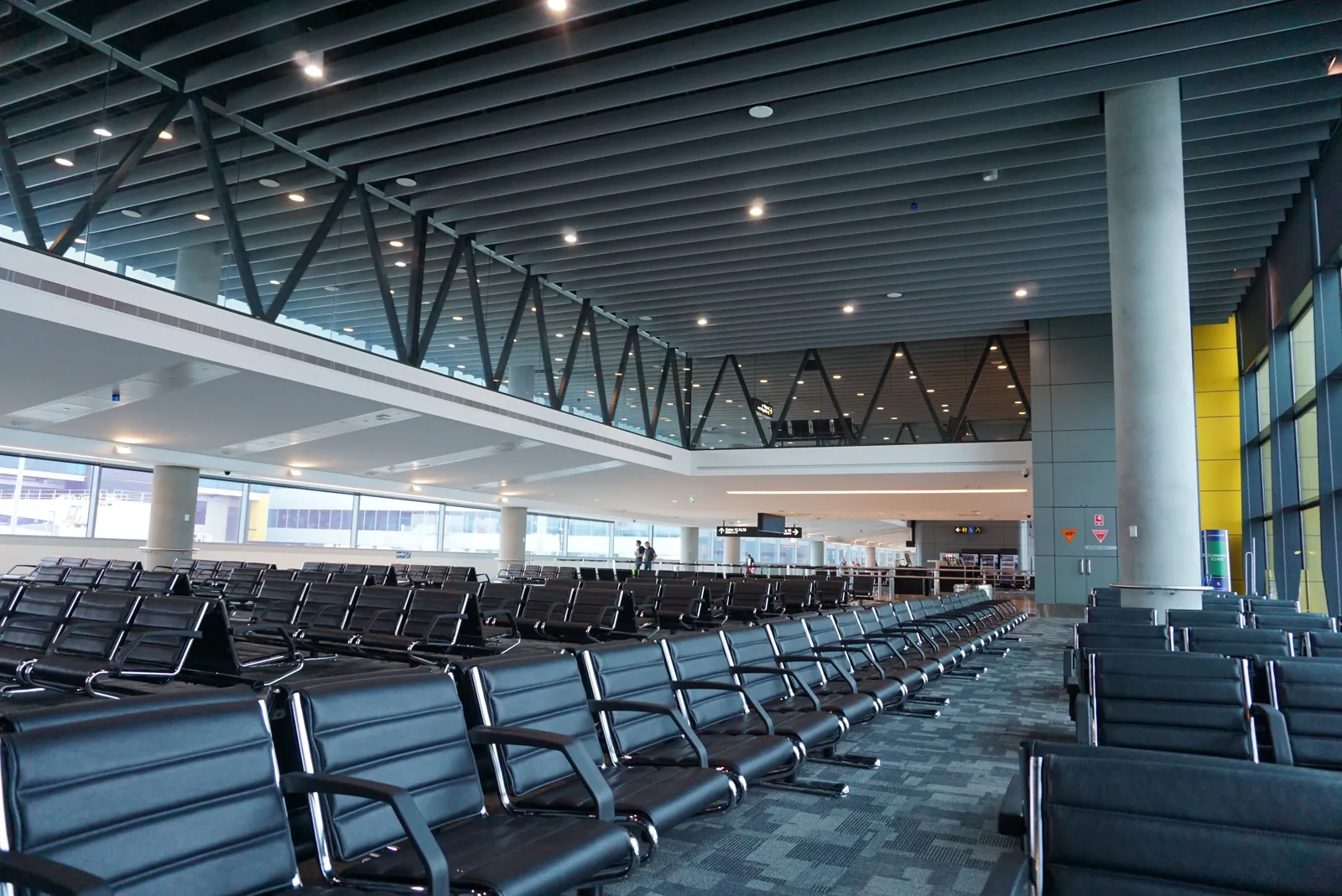 Rows of black seats in a high-ceiling airport terminal, with windows along one side