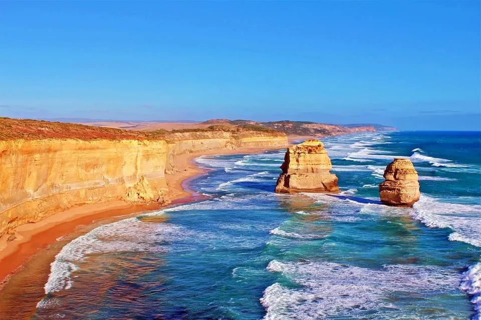 Orange cliffs and limestone stacks rising from a blue sea