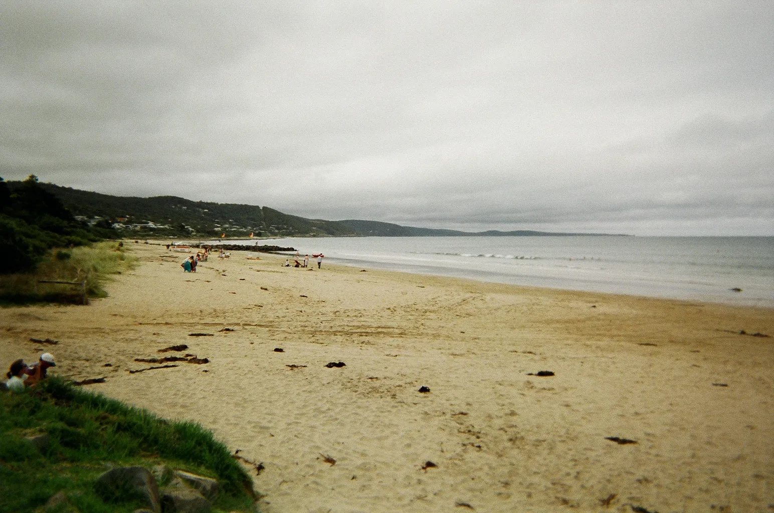 A wide sandy beach and calm sea under a grey sky