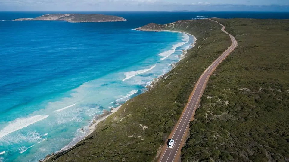 An aerial view of a road running beside a beach and turquoise sea